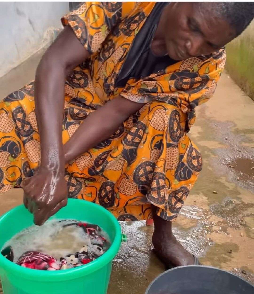 A woman recovering from mental illness is washing her dresses in a green bowl with water.