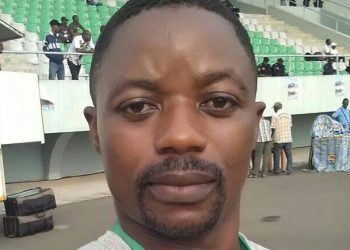 This is a selfie picture of journalist Samuel Wazizi. He is standing in a football stadium, wearing a press badge.