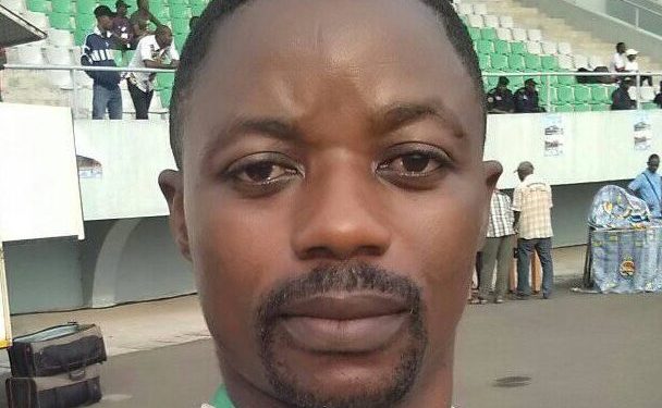 This is a selfie picture of journalist Samuel Wazizi. He is standing in a football stadium, wearing a press badge.