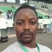 This is a selfie picture of journalist Samuel Wazizi. He is standing in a football stadium, wearing a press badge.
